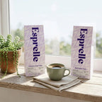 Two Esprelle coffee packages on a wooden surface with a cup of coffee and a plant in the background.